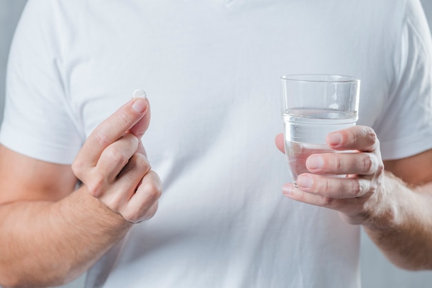 Close-up van een man hand witte pil en glas water in de hand te houden