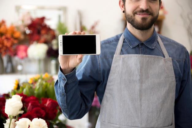 Gratis foto close-up van een mannelijke bloemist die cellphonevertoning in zijn bloemwinkel toont