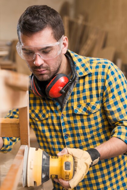 Close-up van een mannelijke timmerman die op het werk hout met behulp van baanschuurmachine oppoetsen