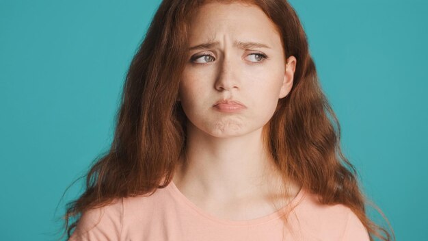 Close-up van een mooi boos roodharig meisje dat beledigd lippen op de camera blaast over een kleurrijke achtergrond Trieste uitdrukking