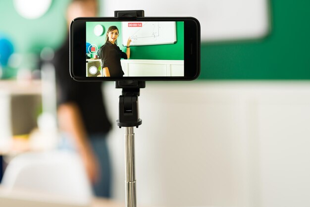 Close-up van een mooie lerares die een livestream op haar smartphone doet om een virtuele klas op de middelbare school les te geven