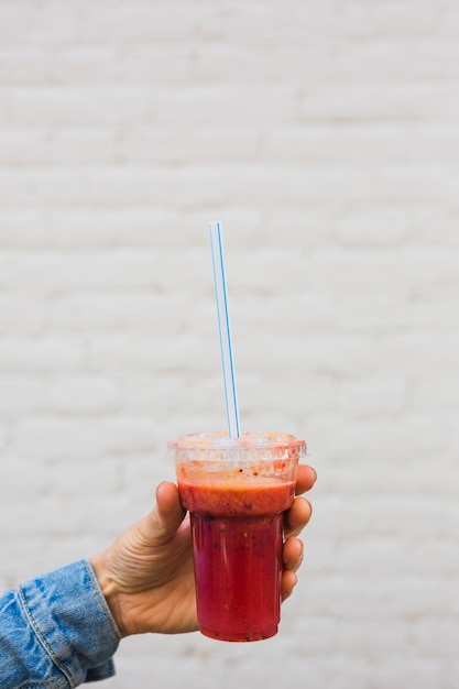 Close-up van een persoon die smoothie in plastic wegwerpbeker met stro