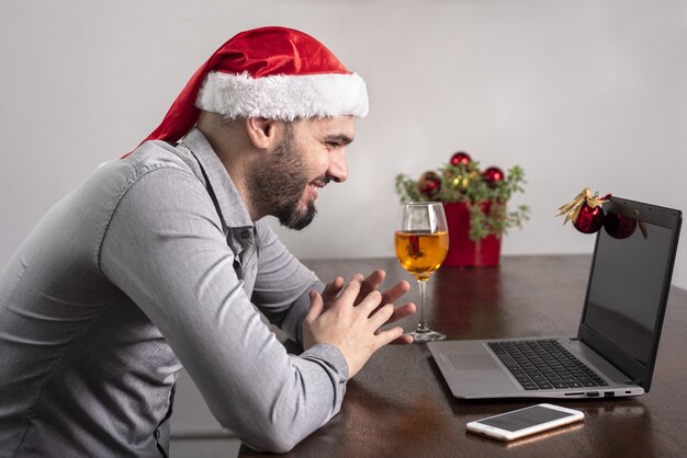 Close-up van een Spaanse man die een kerstmuts draagt, genietend van zijn wijn en een online vergadering heeft