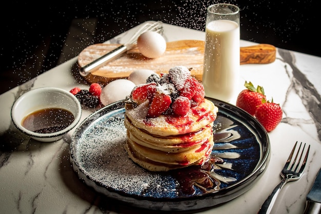 Close-up van een stapel smakelijke pannenkoeken gegarneerd met aardbeien en ingrediënten op de achtergrond