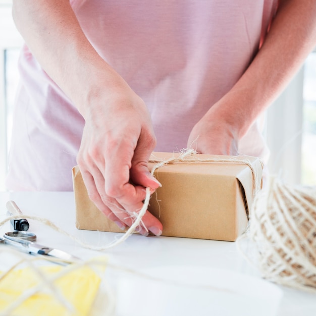 Gratis foto close-up van een vrouw die de draad op bruine ingepakte giftdoos op lijst bindt