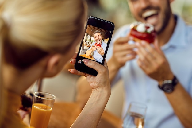 Close-up van een vrouw die een foto maakt van haar vriend die donut eet in een café