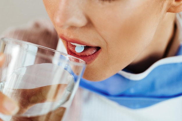 Close-up van een vrouw die een glas water drinkt terwijl ze de pil neemt