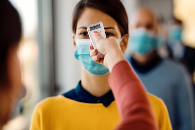 Close-up van een vrouw die haar temperatuur laat meten met een infraroodthermometer als gevolg van een pandemie van het coronavirus