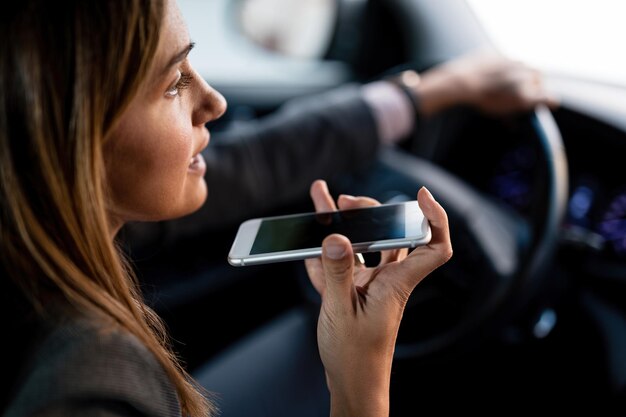 Close-up van een vrouw die mobiele telefoon gebruikt en op de luidspreker praat tijdens het autorijden