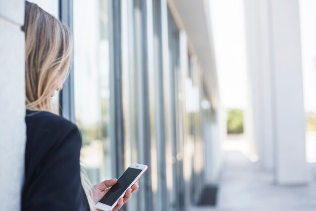 Close-up van een vrouw die op muur leunt die mobiele telefoon met behulp van