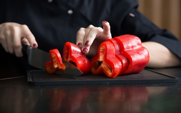 Close-up van een vrouw die rode groene paprika op hakbord met mes snijdt