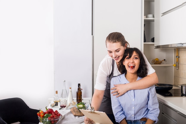 Close-up van een vrouw die van zijn vriend houdt die recept op klembord in de keuken bekijkt