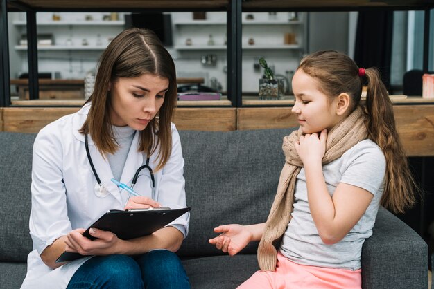 Close-up van een vrouwelijke arts die op klembord schrijft die ziek meisje diagnostiseert