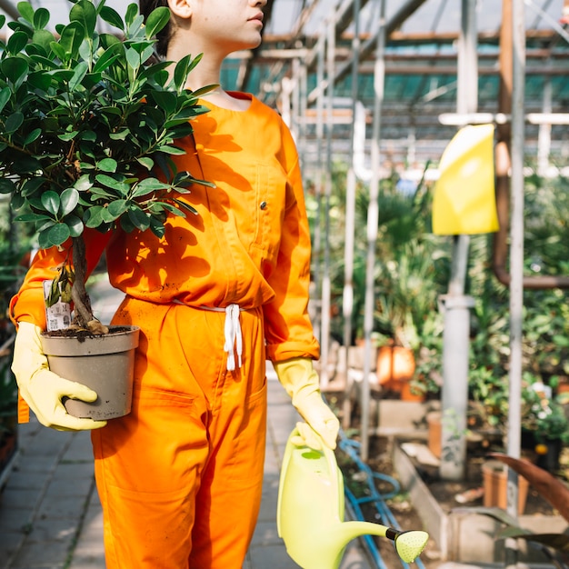 Close-up van een vrouwelijke tuinman die in werkkleding ingemaakte installatie en gieter houdt