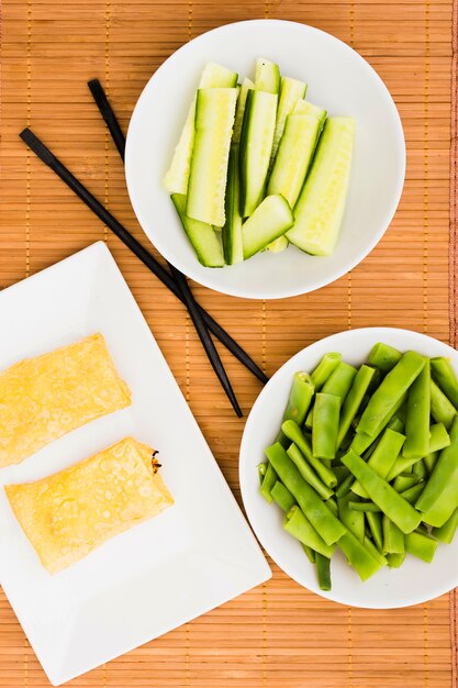 Close-up van gefrituurde loempia&#39;s in lade met courgette plakjes en platte bonen op placemat