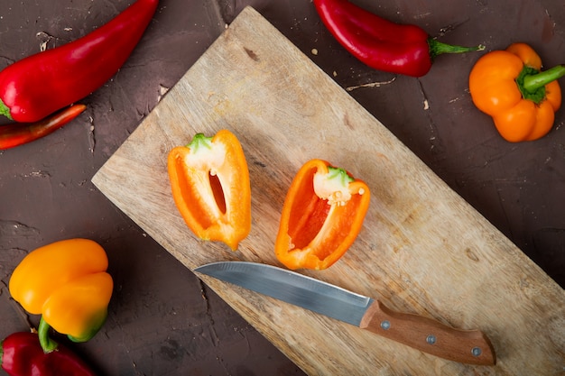 Gratis foto close-up van gesneden peper op houten oppervlak met mes en paprika op kastanjebruine achtergrond