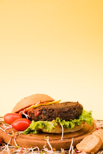 Close-up van hamburger met vrolijke tomaten; brood en sla op gele achtergrond