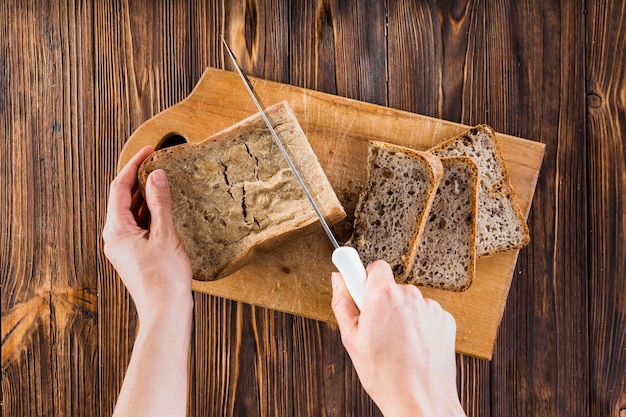 Gratis foto close-up van hand die het brood van brood met mes op hakbord snijdt