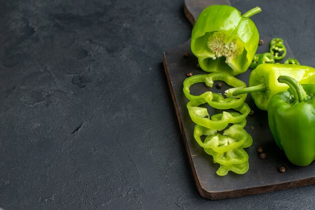 Close-up van hele gesneden gehakte groene paprika's op donkere houten snijplank aan de linkerkant op zwart oppervlak black