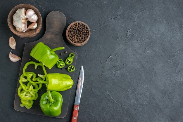 Close-up van hele gesneden gehakte groene paprika's op donkere houten snijplank aan de rechterkant op zwart oppervlak