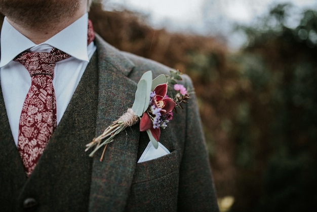 Close-up van het kostuum van een bruidegom met bloemen en rood gevormde stropdas met bomen op de achtergrond