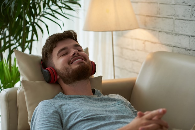 Close-up van hipsterkerel het ontspannen op zijn bank die aan muziek luistert