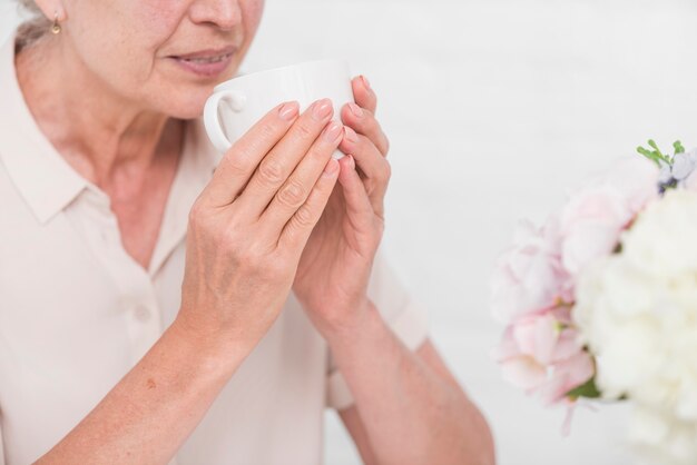 Close-up van hogere vrouw die witte kop van koffie houdt