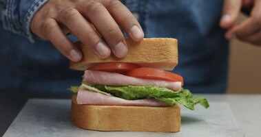 Close-up van iemands hand die sandwich maakt, legt van kanten alle ingrediënten op plaat