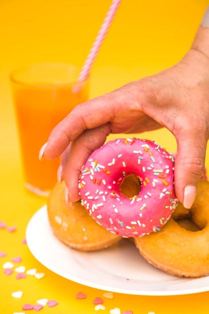 Gratis foto close-up van iemands hand oppakken van roze donut van plaat