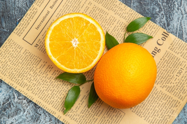 Close-up van in tweeën gesneden en hele verse sinaasappel met bladeren op krant op grijze achtergrond stock foto
