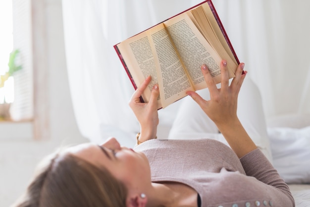 Gratis foto close-up van jonge vrouw die op het boek van de bedlezing ligt