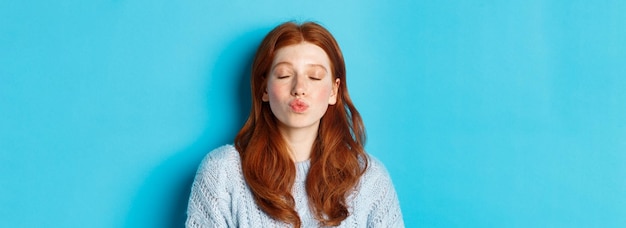 Gratis foto close-up van jonge vrouw met rood golvend haar die zich met gesloten ogen en getuite lippen bevindt die op ki wachten