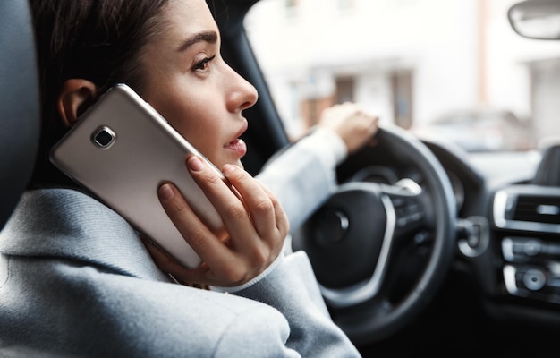 Close-up van jonge zakenvrouw die naar kantoor rijdt en iemand aan de telefoon belt Vrouw die op de chauffeur zit en op smartphone praat