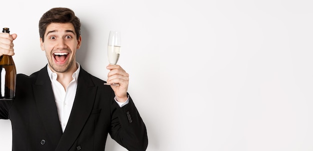 Close-up van knappe glimlachende man in zwart pak die een maakt met champagne en glas vieren | Gratis Foto