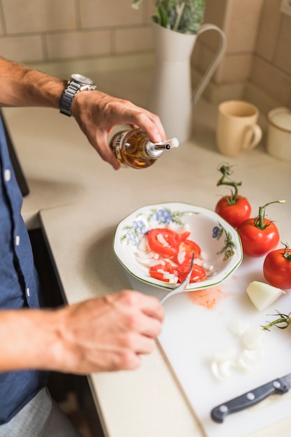 Close-up van man's hand dressing de salade met olijfolie in de keuken