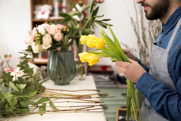 Close-up van mannelijke bloemist die de gele tulpen in de bloemwinkel schikken