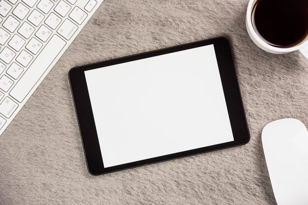 Close-up van moderne digitale tablet met toetsenbord; koffiekopje en muis op grijze achtergrond