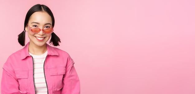 Close up van mooie Aziatische vrouwelijke model in stijlvolle zonnebril poseren tegen roze achtergrond in trendy outfit kopie ruimte