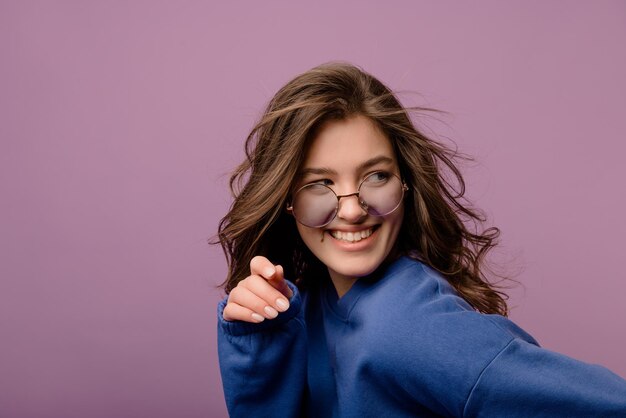 Close-up van mooie jonge blanke brunette meisje in blauwe hoodie en bril kijkt weg in studio Mensen emoties levensstijl en mode concept