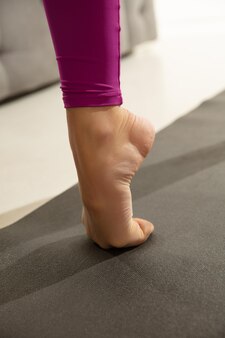 Close up van mooie jonge vrouw die binnenshuis aan het trainen is en yoga-oefening doet op grijze mat details