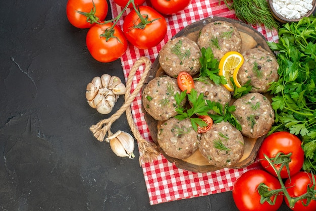 Close-up van ongekookte gehaktballen op een houten snijplank op rode gestripte handdoek en tomaten knoflook aan de linkerkant op donkere achtergrond