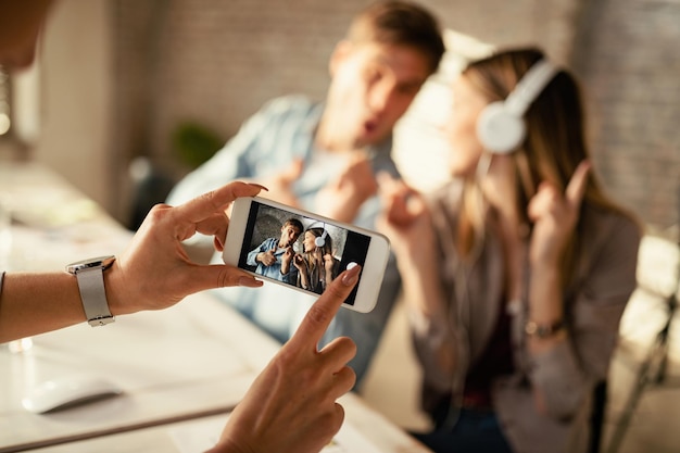 Close-up van onherkenbare vrouw die een foto neemt met smartphone van speelse collega's op kantoor