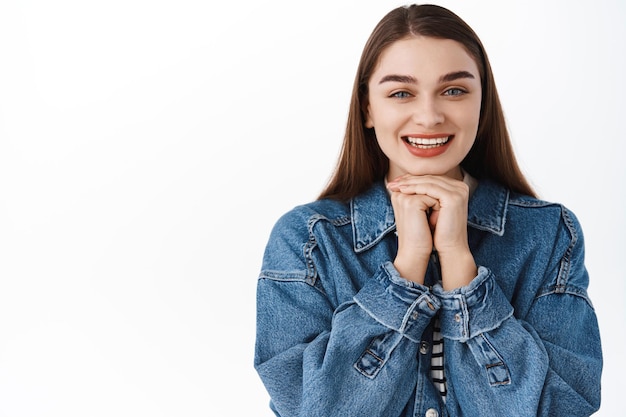 Close up van opgewonden schoonheid meisje hand in hand onder het gezicht en glimlachen, vragen om iets, zeg alsjeblieft, hoopvol en opgetogen kijken, dagdromen, staande op witte achtergrond