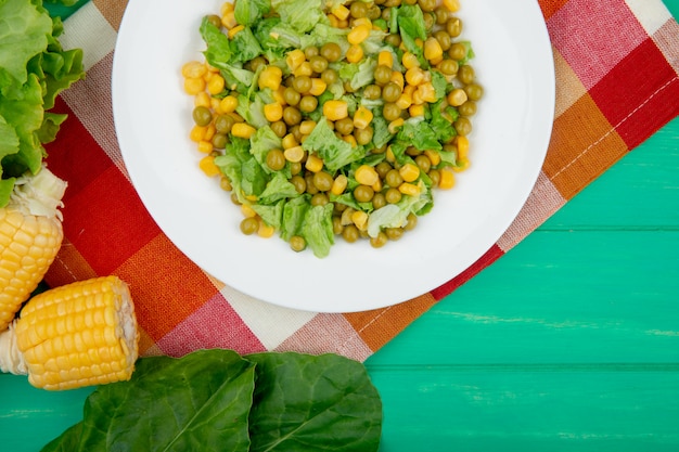 Gratis foto close-up van plaat van gele erwt en gesneden sla met maã¯s spinazie sla op doek en groene tafel