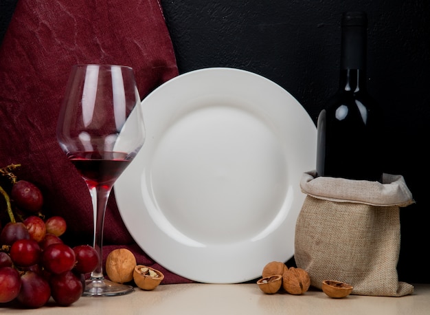 Close-up van rode wijn en lege plaat met druiven en walnoot op witte ondergrond en zwarte achtergrond