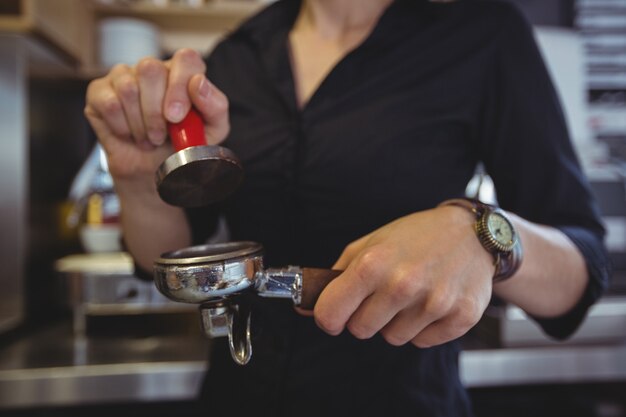 Close-up van serveerster die een sabotage gebruiken om gemalen koffie in een portafilter te drukken
