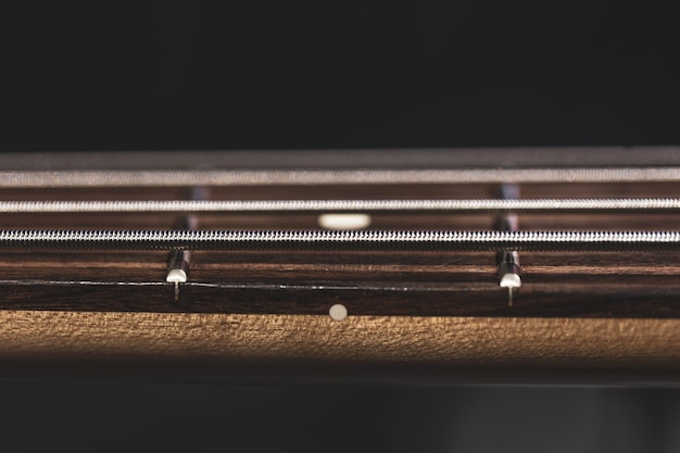 Gratis foto close-up van snaren op de toets van een basgitaar op een wazige donkere achtergrond.