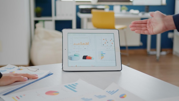 Close-up van tablet en papieren met gegevensgrafieken op bureau die door collega's worden gebruikt voor bedrijfsontwikkeling. Bedrijfscollega's die aan projectpresentatie werken voor management- en marketingstrategie