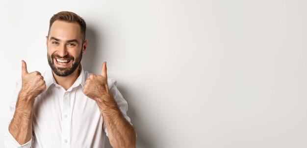 Close-up van tevreden bebaarde man in wit overhemd met duimen omhoog in goedkeuring zoals en positief mee eens