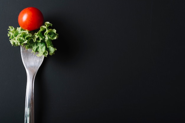 Close-up van tomaat en sla met vork op zwarte achtergrond
